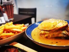 Franceshina sandwich in sauce on a white plate witha portion of french fries