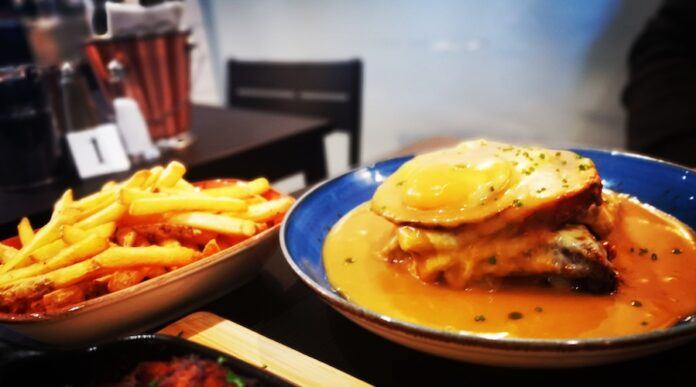 Franceshina sandwich in sauce on a white plate witha portion of french fries