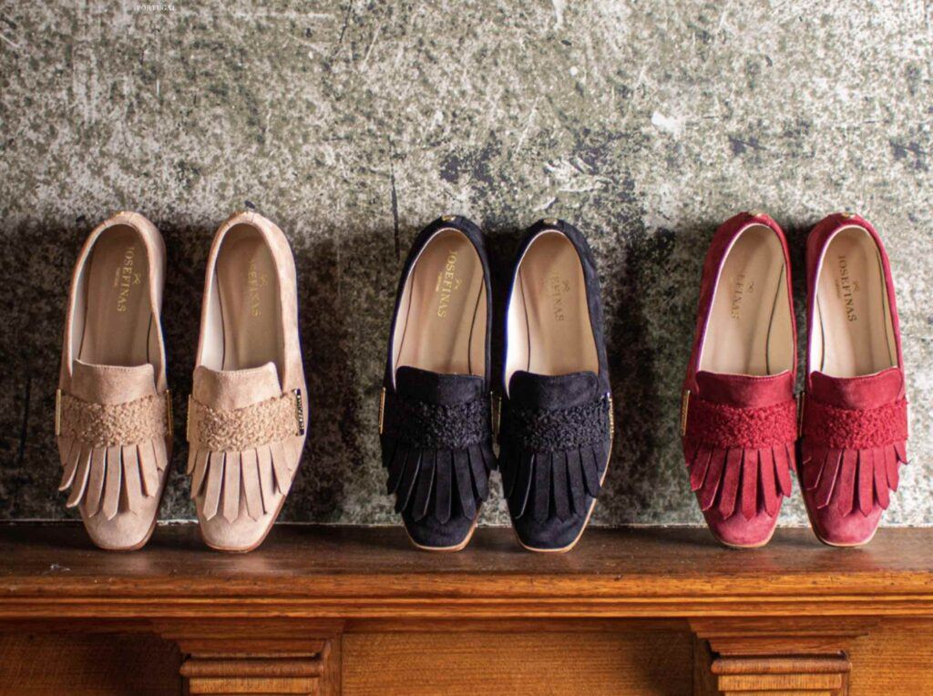 Three pairs of shoes, stood on their toes, on a sideboard, lean against a a wall.