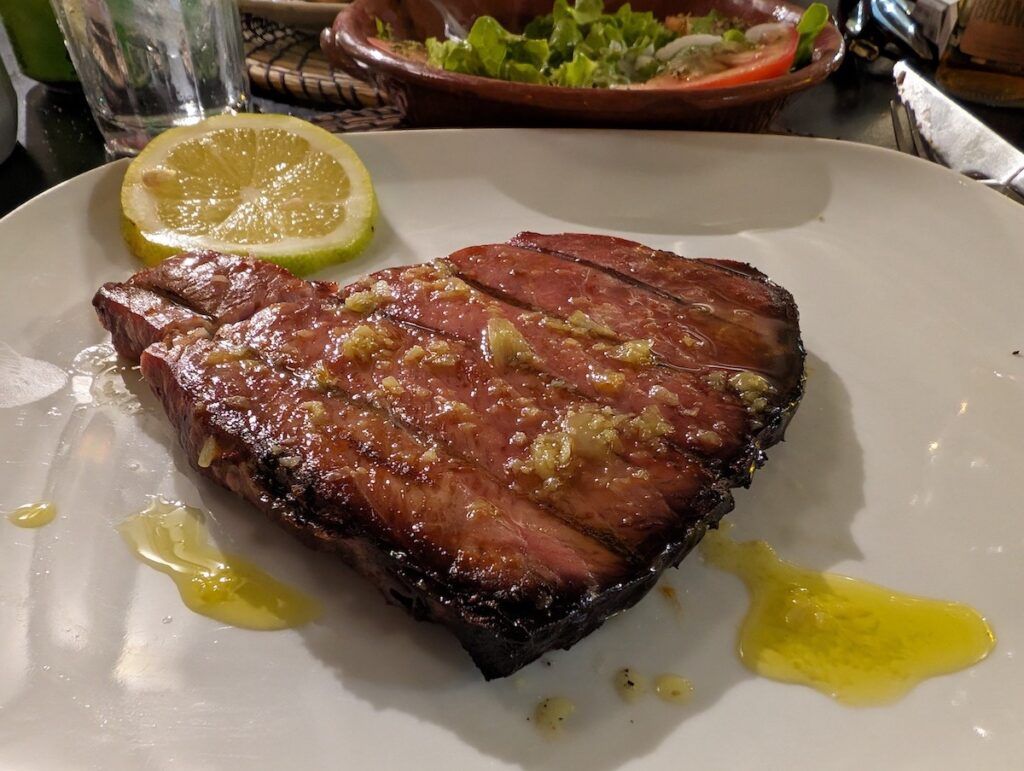 A tuna steak on a plate with a slice of lemon garnished with garlic and butter