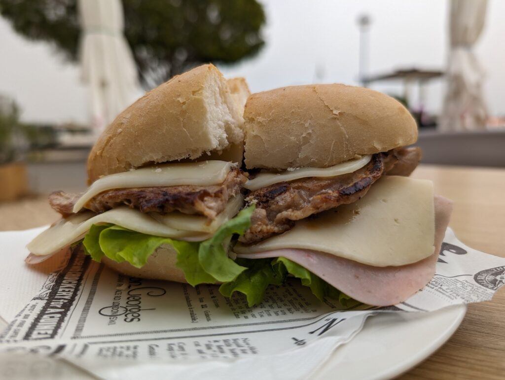 A bifana sandwich served on a white plate outdoors