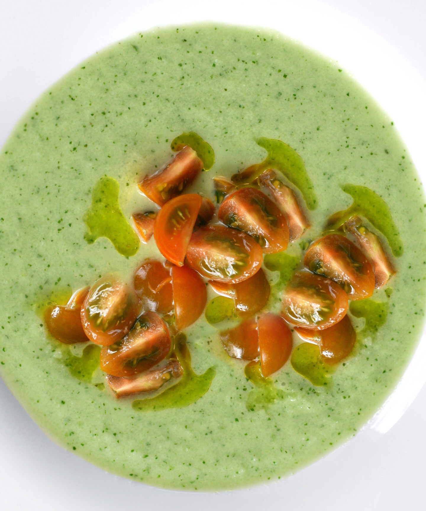 A serving of caldo verde , a green soup in a bowl, topped with tomatoes.