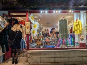 A vintage shop window photographed in the evening as a woman in black walks in to the store