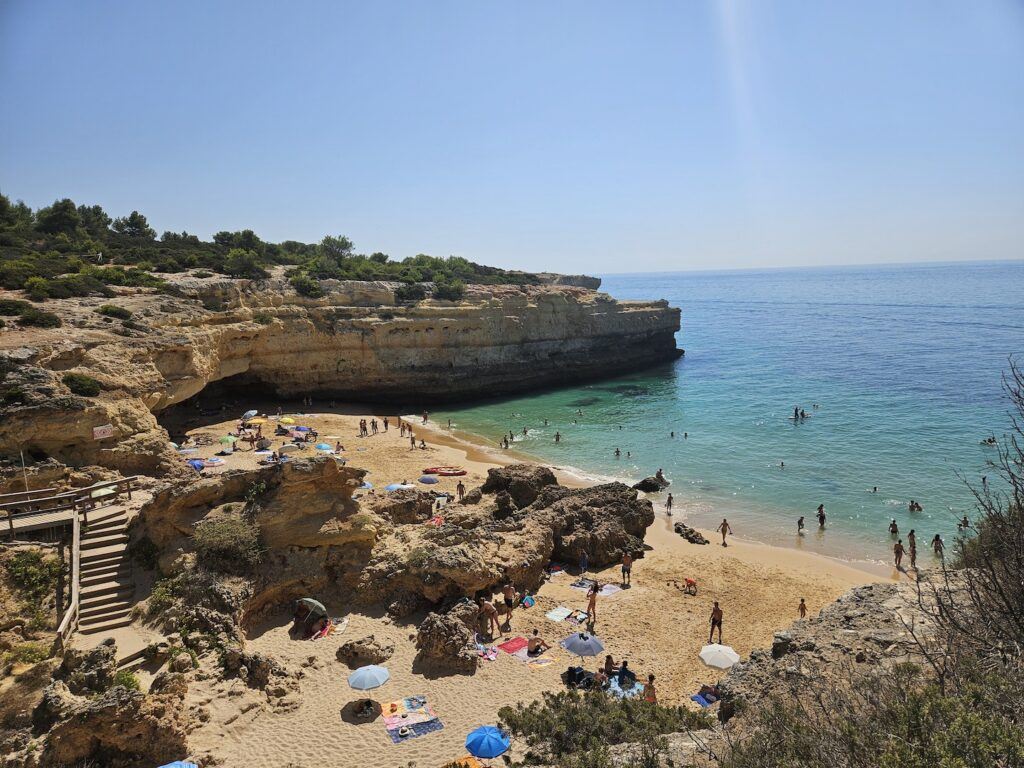 A small Algarve beach seen from a clifftop with people on the beach and bathing