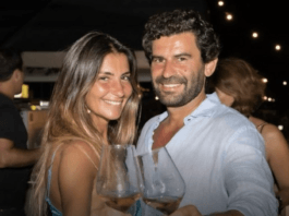 A happy celebrity couple in a nightclub standing close together smiling at the camera and holding wine glasses