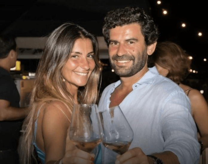 A happy celebrity couple in a nightclub standing close together smiling at the camera and holding wine glasses