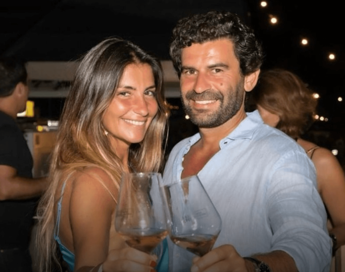 A happy celebrity couple in a nightclub standing close together smiling at the camera and holding wine glasses