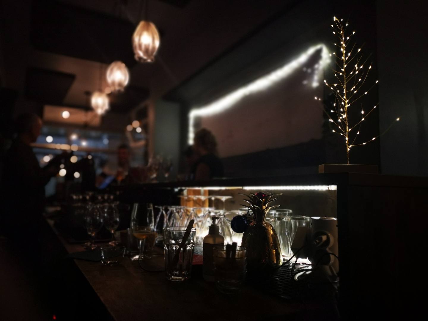 A dimly lit bar counter with glasses and decorative lights