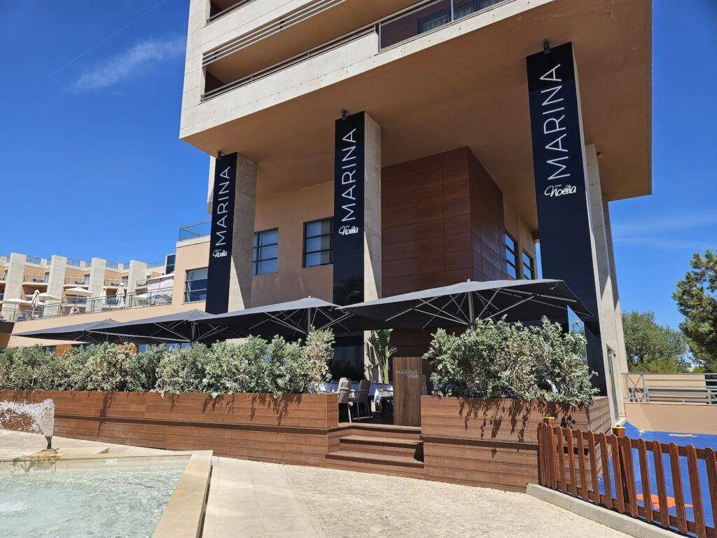 A restaurant, with hoarding saying Noelia at the Marina, seen against a blue sky