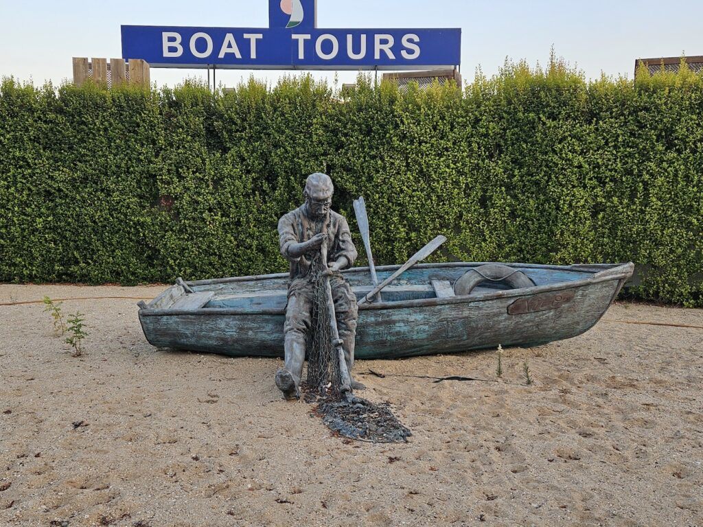 A sculpture of a fisherman and a boat with a sign advertising boat tours in Portugal