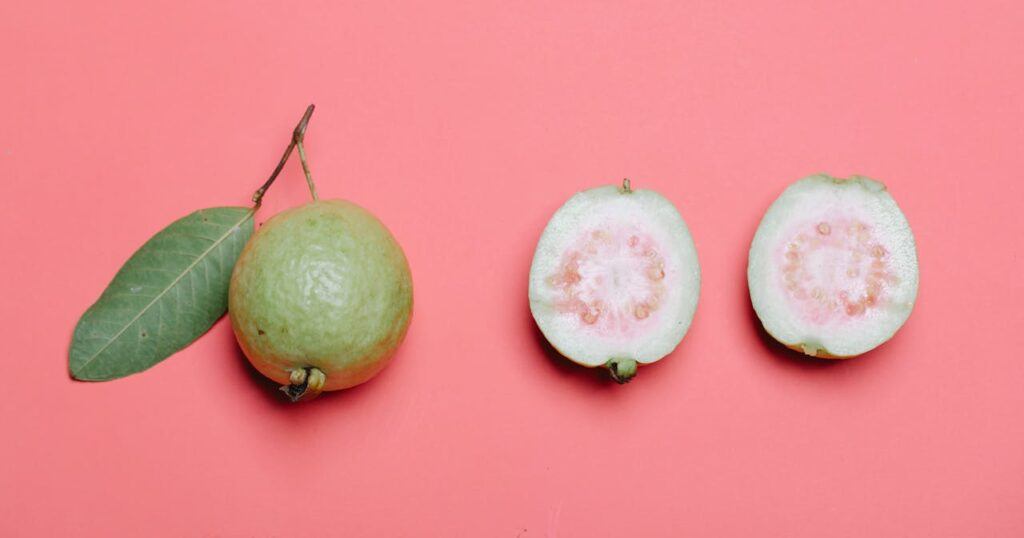 One whole, and one cut guava fruit on a plain, pink background