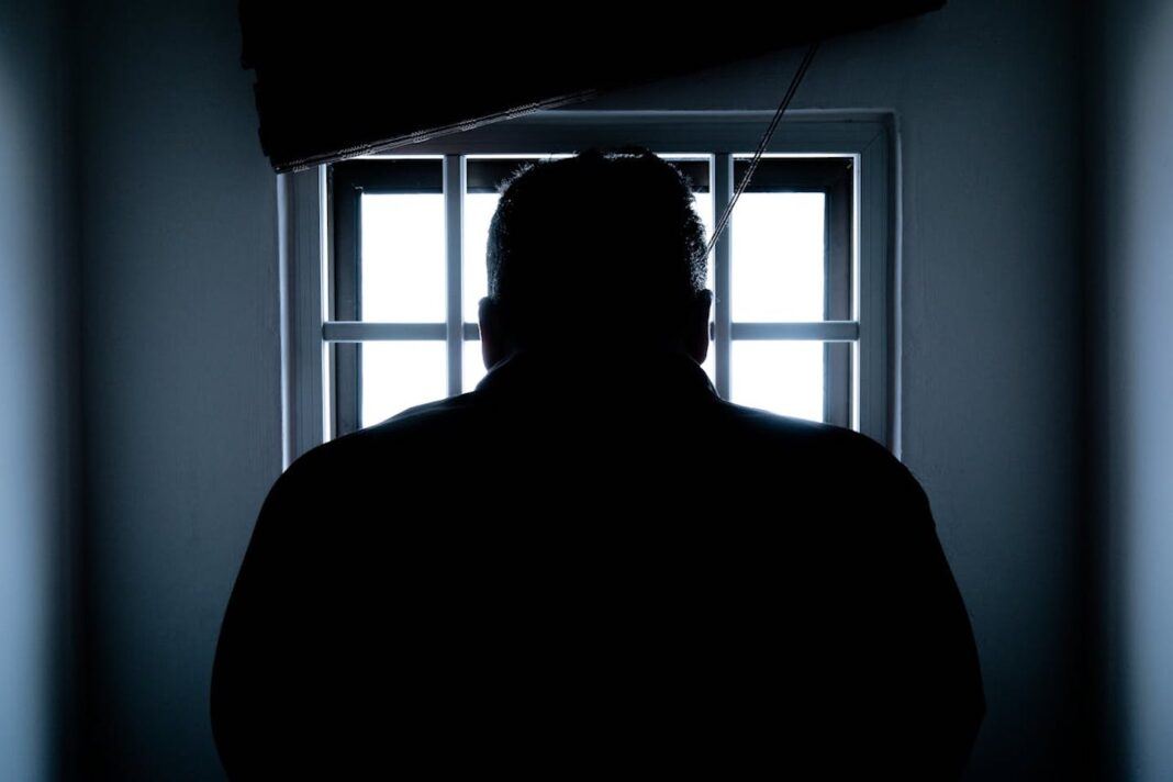 A prisoner looks through the bars of a darkened jail cell