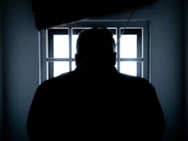 A prisoner looks through the bars of a darkened jail cell