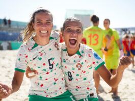 Two women in Portuguese football jerseys smile and grimace for teh camera.