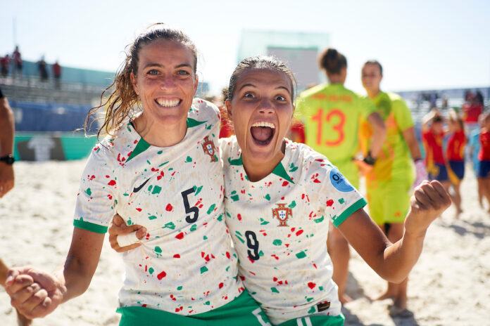 Two women in Portuguese football jerseys smile and grimace for teh camera.