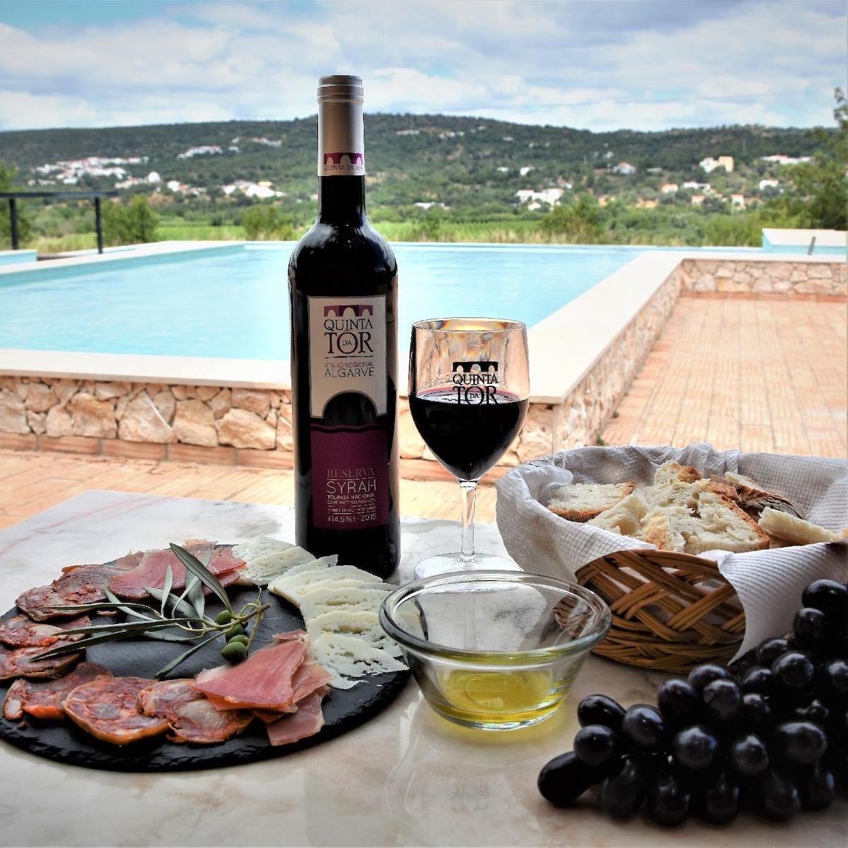 A glass of red wine and some tapas on a board beside a swimming pool