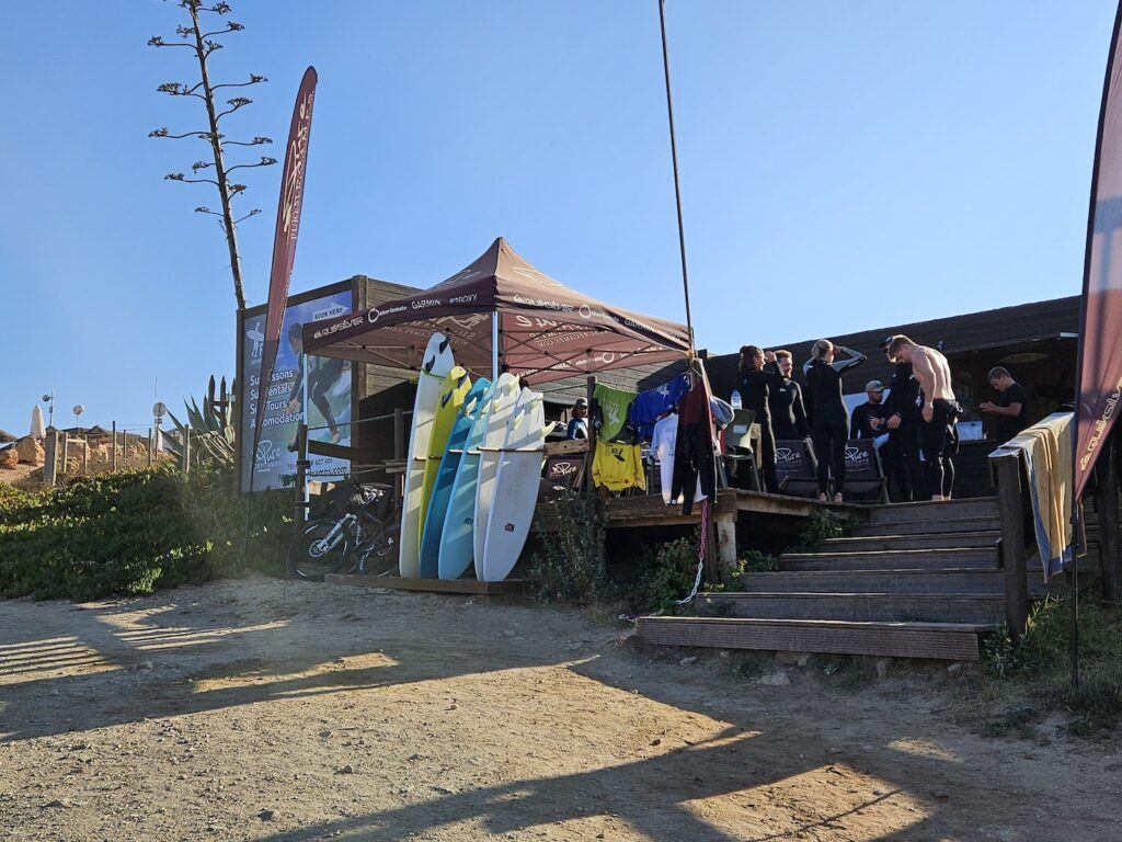 Surfers get ready at a surf-school with a sandy beach in teh foreground