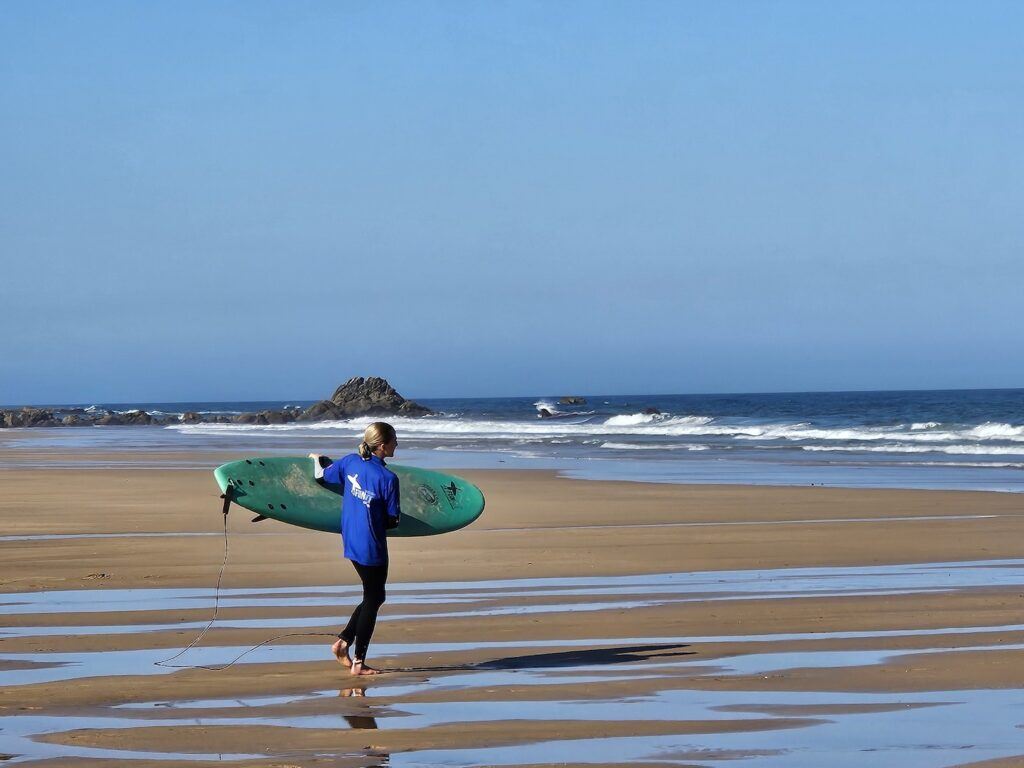 A female surfer carries a surfboard towards the sea on a beach in Sagres, Potugal.