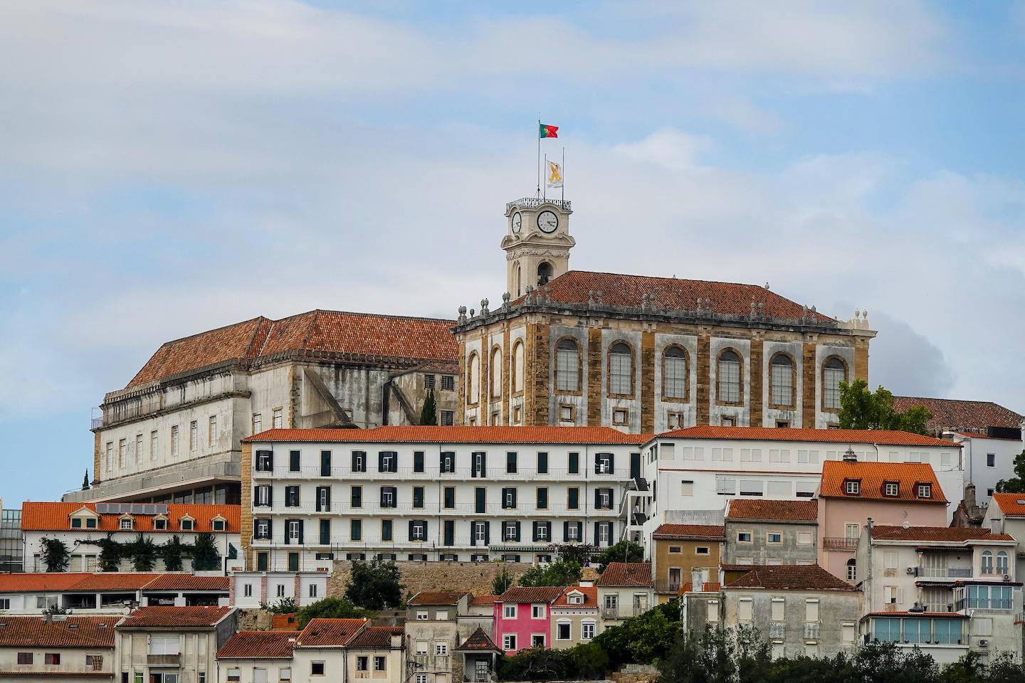 A medieval building, of the University of Coimbra seen on a hill, surrounded by the town of Coimbra.