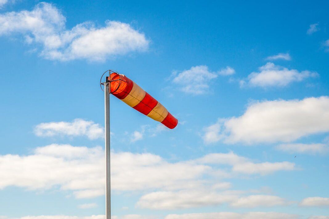 A red and yellow windsock blowing in the wind, with a scattering of clouds in the distance