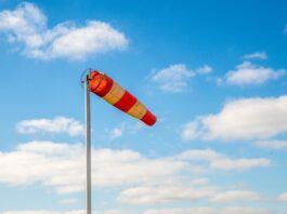 A red and yellow windsock blowing in the wind, with a scattering of clouds in the distance