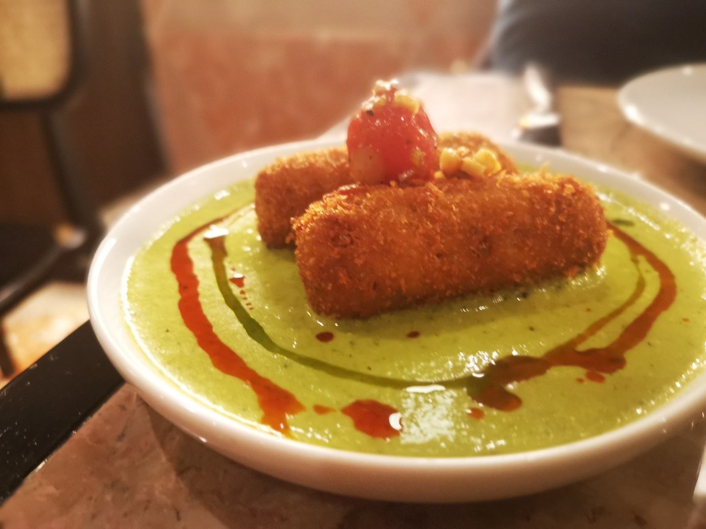 Two Portuguese croquettes, on a plate decorated in a modern style with a green sauce with dribbles of soy sauce.