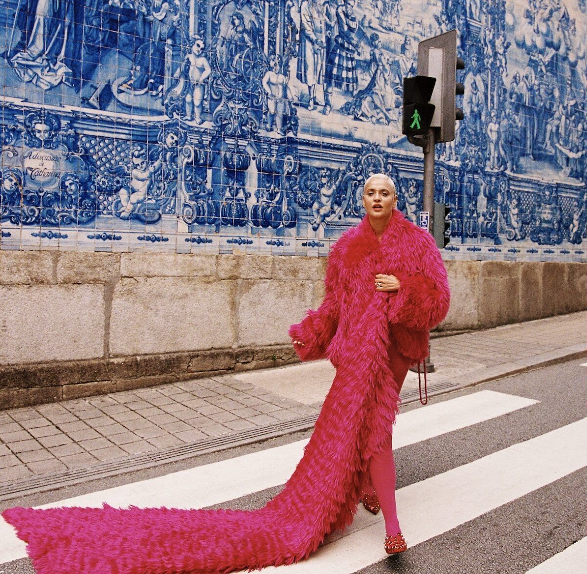 Singer Mariza poses in a long red dress in front of a tiled outside decorative wall