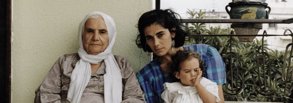 A promotional still from a film shows an older woman and a younger woman seated, holding an infant child.