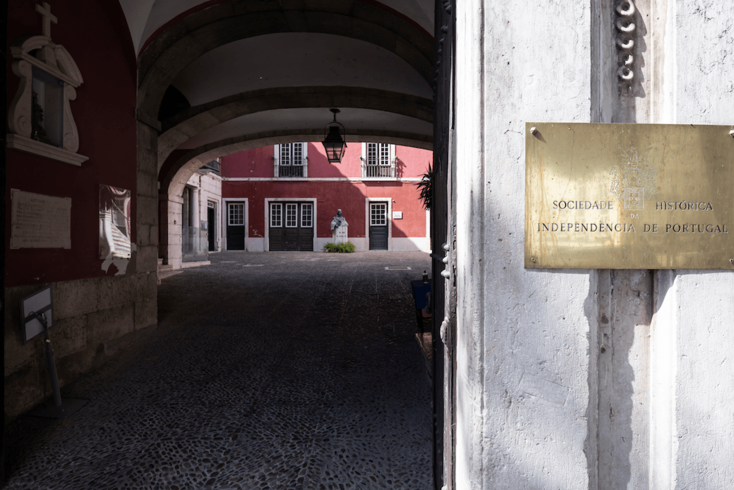 Exterior view of the Palácio da Independência through a short archway with a brass name plaque visible in the foreground.