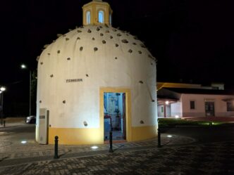 An ancient small church in Portugal, seen at night, with stones in its roof and illuminated by lights