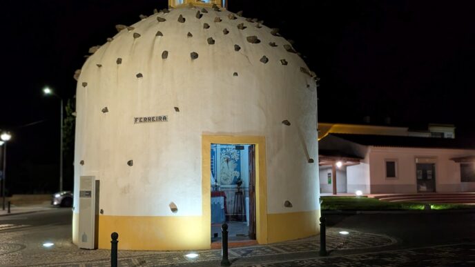 An ancient small church in Portugal, seen at night, with stones in its roof and illuminated by lights