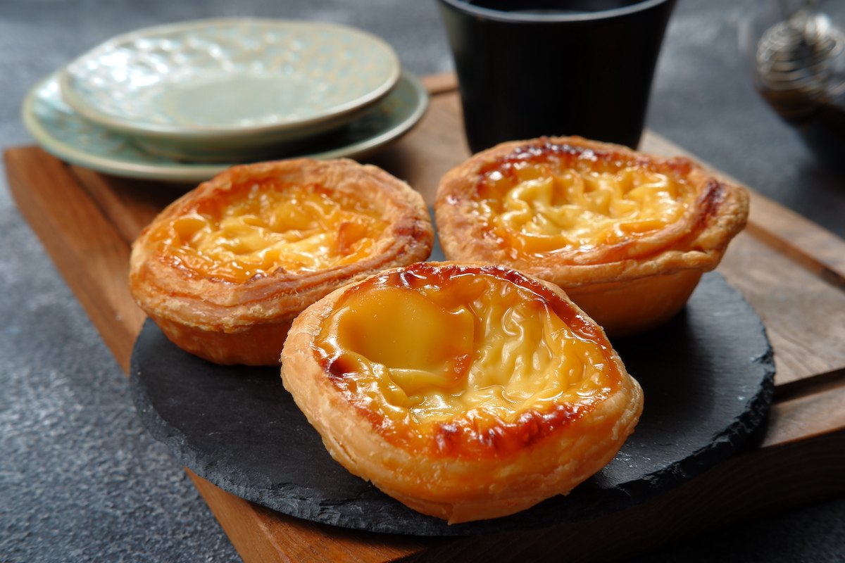 Three custard tarts on a place, with a cup of black coffee visible behind them.