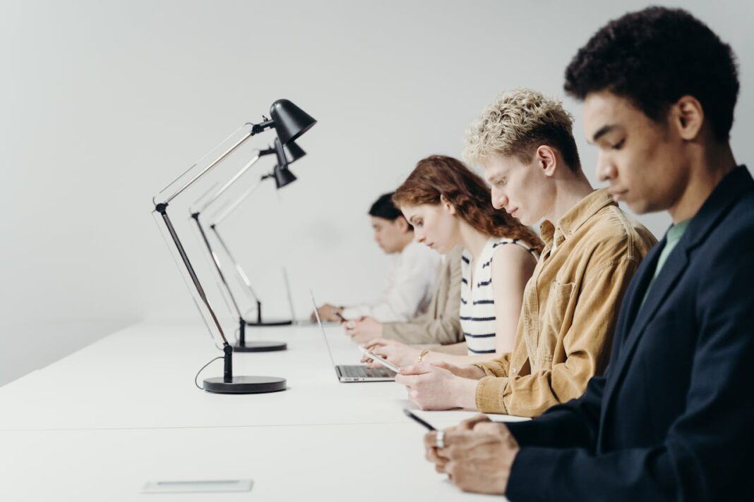 Young people sitting at a desk working on laptops and phones.