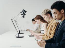 Young people sitting at a desk working on laptops and phones.