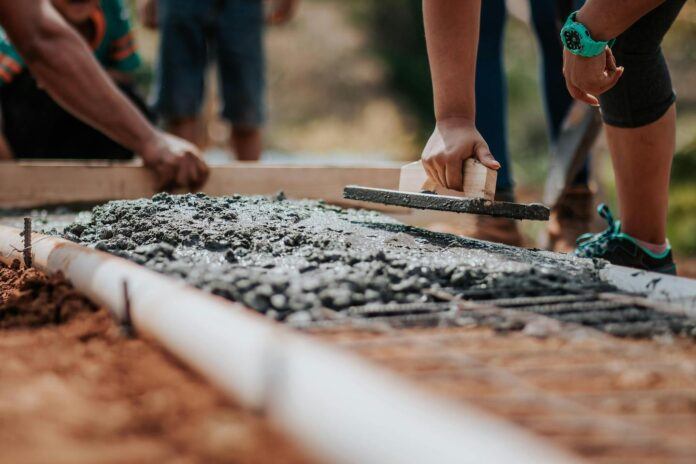 Construction workers hands are seen platering cement at ground level.