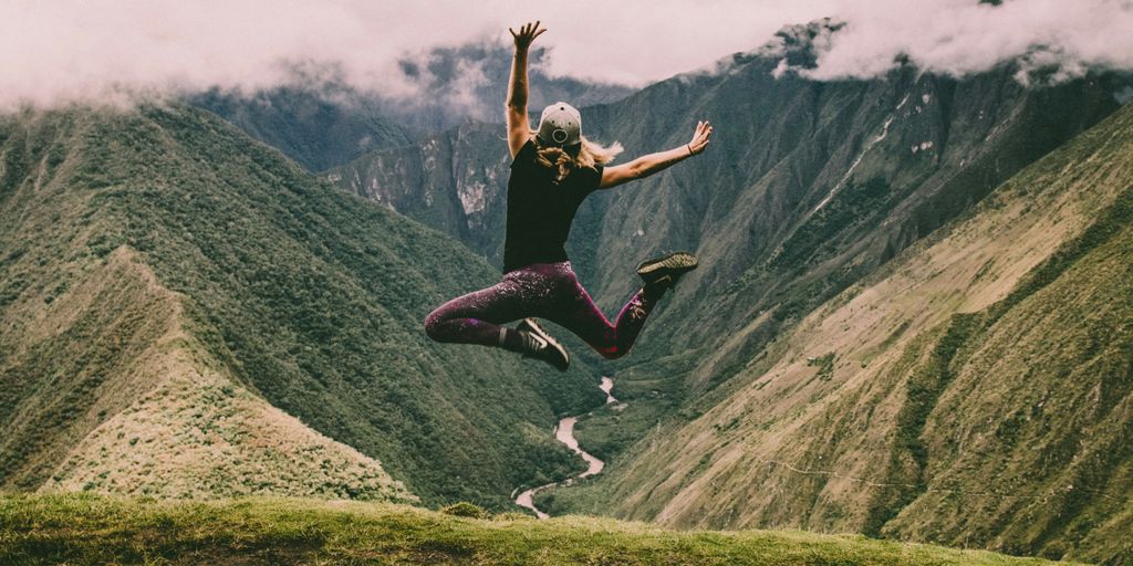 woman jumping on green mountains