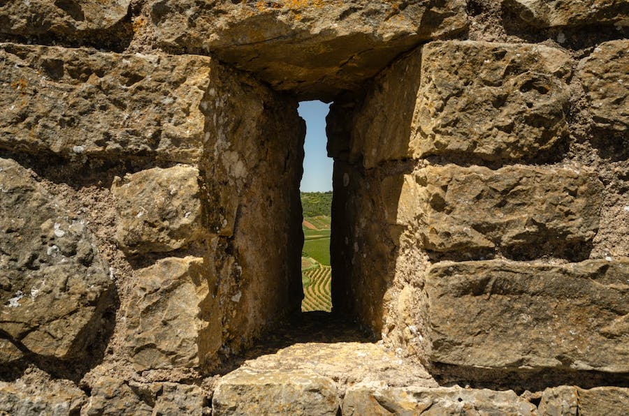 A view froma castle window with green fields seen through the small, slit window.