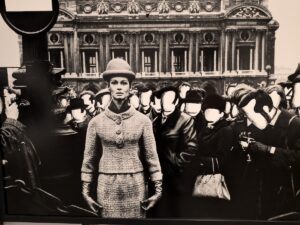 A photo by William Klein of a model standing with a bowler hat surrounded by unseen men