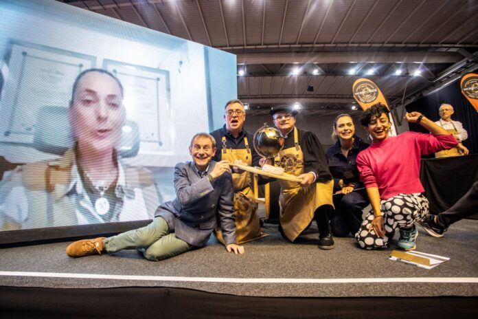 A group of people gather on a stage, while a video screen shows a close up of a woman in teh background.