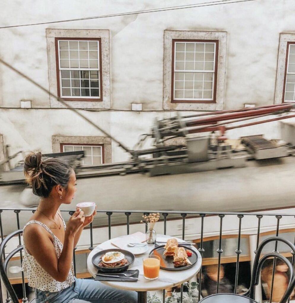 A woman holds a coffee cup with both hands at an outdoor cafe