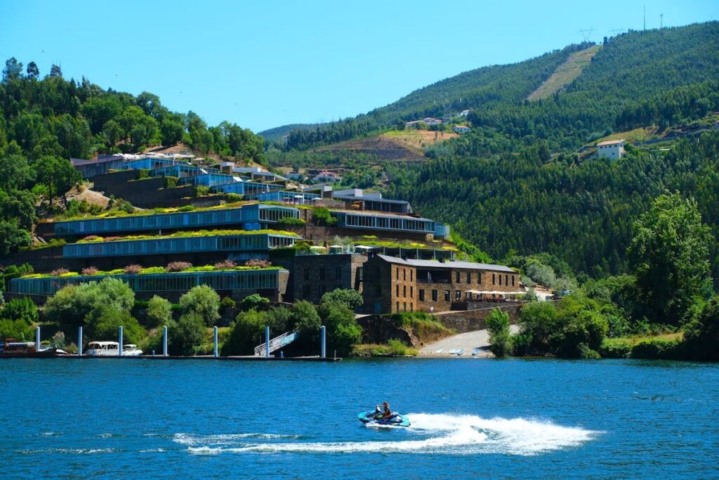 An tiered hotel on a hill in Portugal seen with the Douro River in the foreground where a person rides a jet-ski on the river
