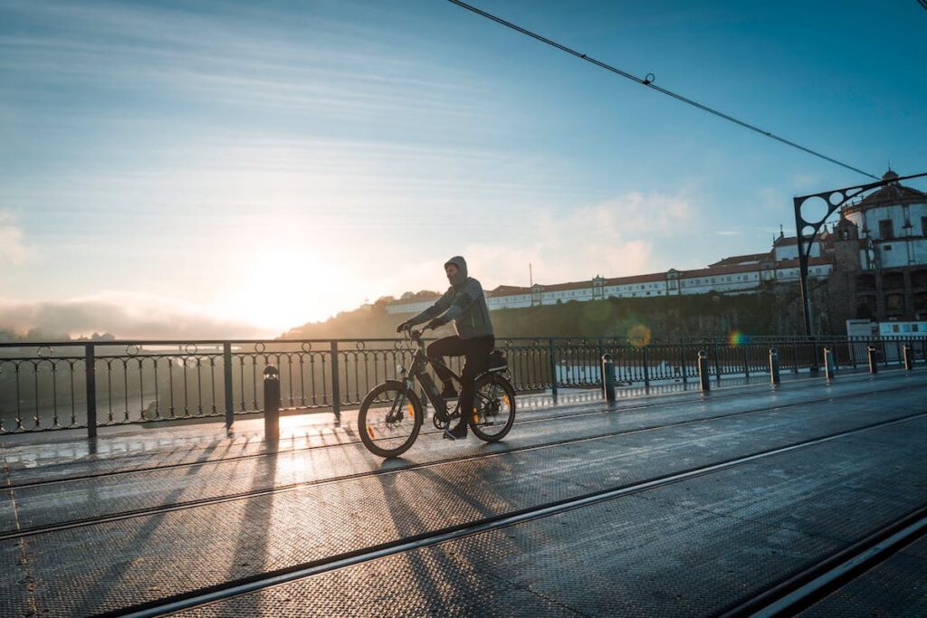 A person cycles over a small bridge in Lisbon with the evening sun setting in the background