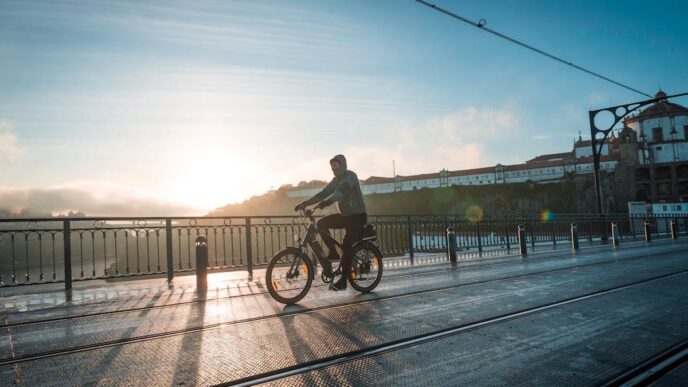 A person cycles over a small bridge in Lisbon with the evening sun setting in the background