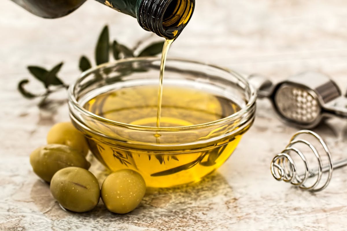 Olive oil in a bowl, seen with some green olives beside the bowl.