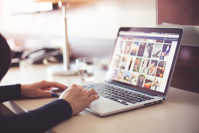 A person's hands are visible on a laptop with pictures out of focus on th screen.