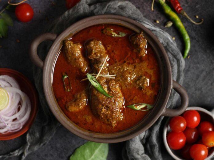 A bowl of vindaloo curry in a dish, seen from above, on a table sith accoutrements