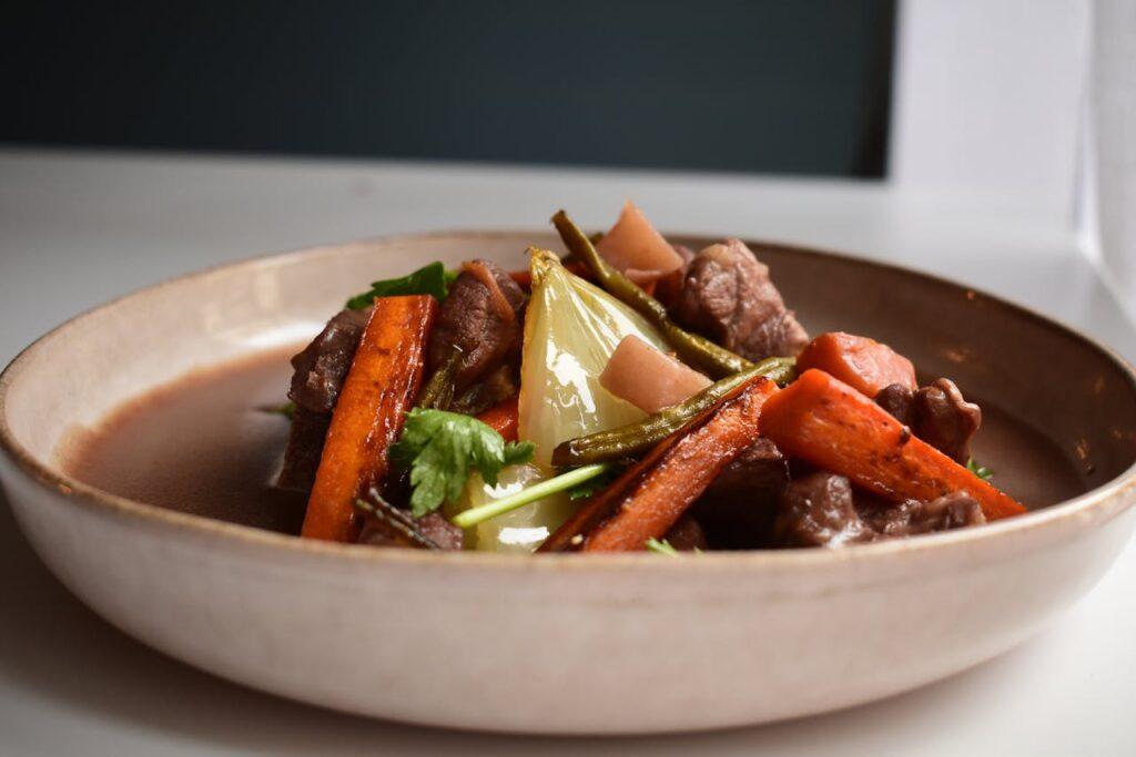 Stewed beef and vegetables in a white dish, on a table.