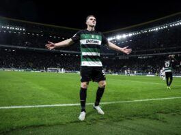 Viktor Gyokeres stands in a Sporting Lisbon jersey on a football with with his arms outstretched.