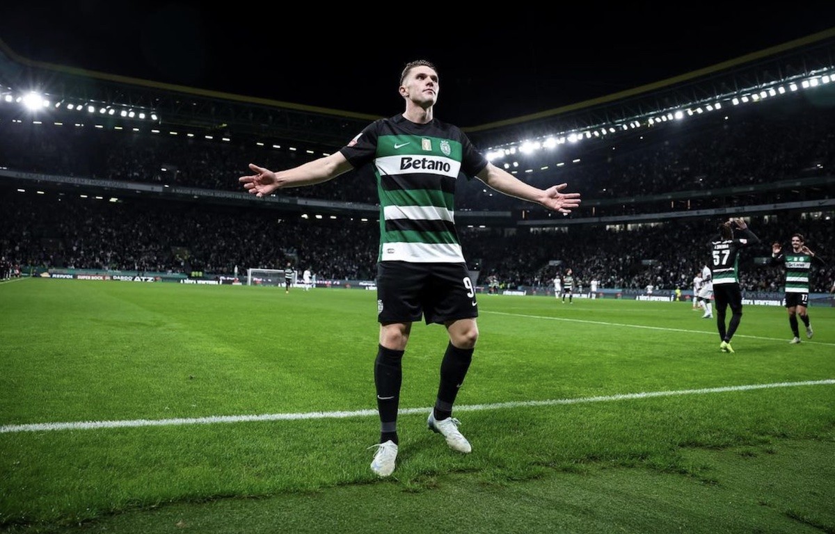 Viktor Gyokeres stands in a Sporting Lisbon jersey on a football with with his arms outstretched.