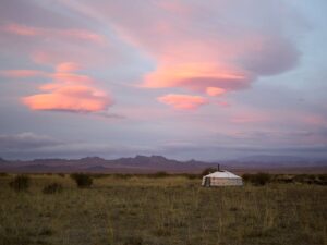 A yurt is seen in the distance in a field, with an evening sky above.